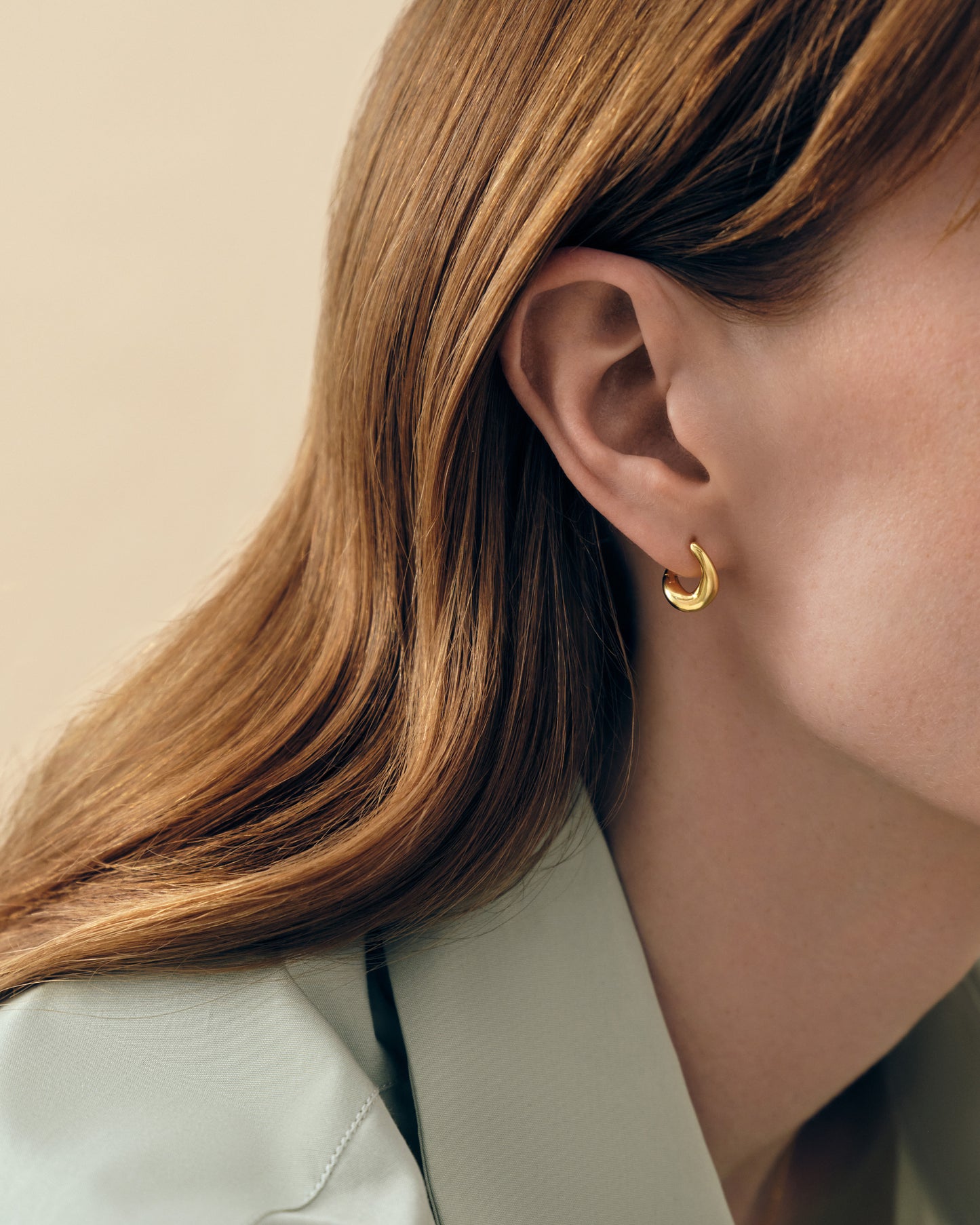 Close-up of a woman wearing Charlotte Collins Small Twist Hoop Earrings, showcasing gold-plated twisted huggie hoops, crafted from recycled metals for considered everyday fine jewellery.