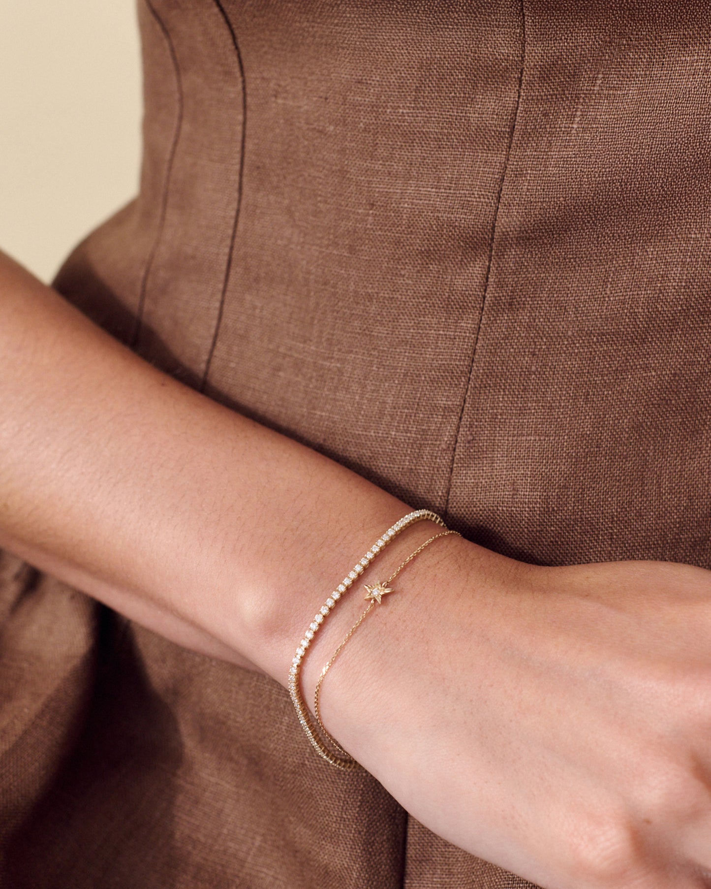 Close-up of a wrist wearing a Solid Gold Lab-Grown Diamond Tennis Bracelet alongside a delicate gold chain with a small star charm, showcasing fine 14ct gold jewellery made from recycled metals.
