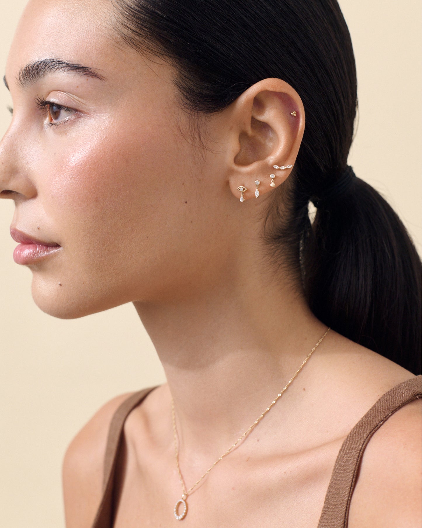 Woman wearing a Solid Gold Lab-Grown Marquise Diamond Piercing Earring along with multiple stud earrings and a delicate gold necklace, showcasing fine jewellery crafted from recycled metals with ethical sourcing.