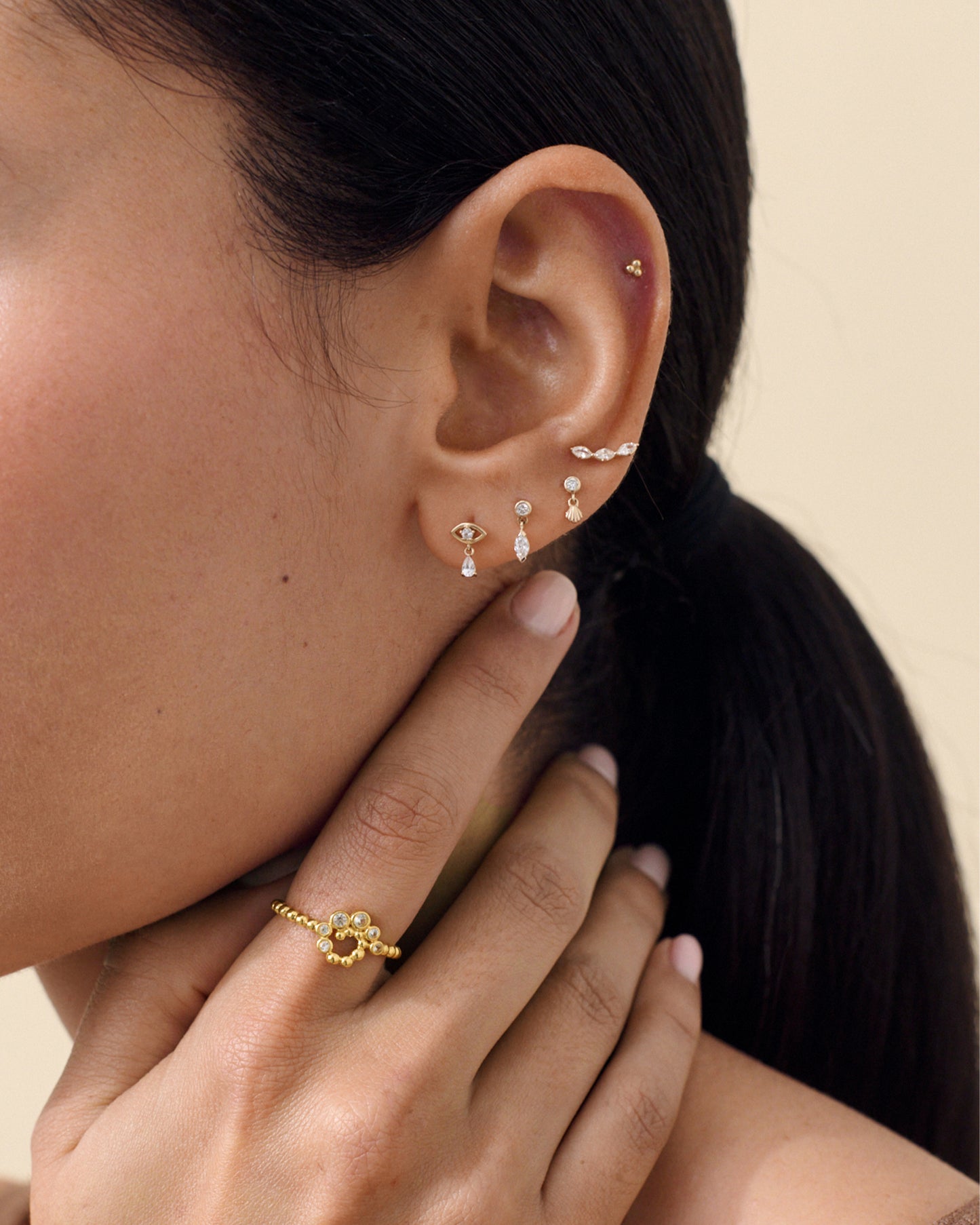 Close-up of a woman wearing a Solid Gold Lab-Grown Marquise Diamond Piercing Earring and other stud earrings, featuring fine jewellery crafted from recycled metals and lab-grown diamonds.