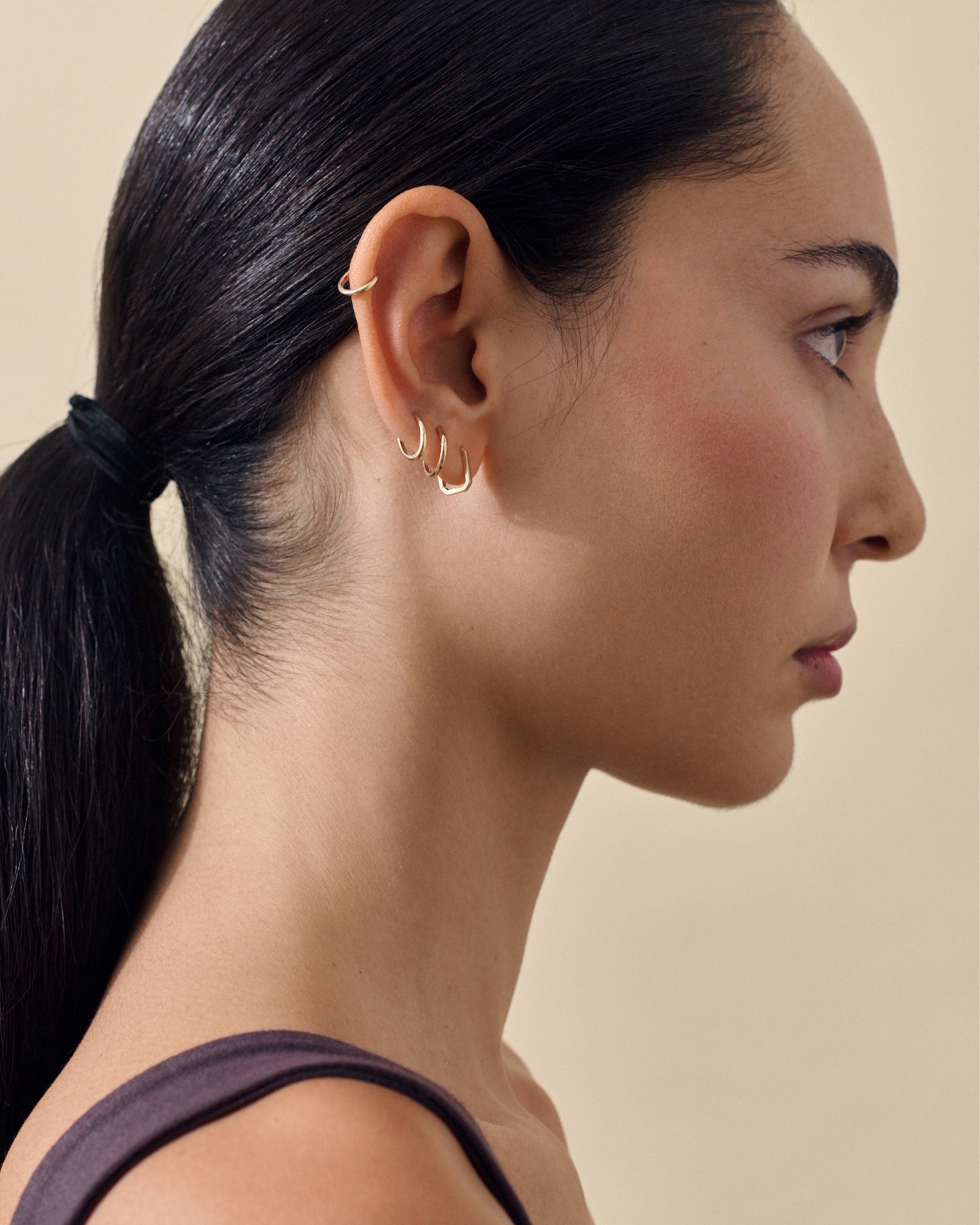 Profile view of a woman wearing Solid Gold Mini Huggie Hoop Earrings with multiple small gold hoop earrings along the ear, showcasing sustainable, finely crafted solid 14ct gold jewellery made from recycled metals.