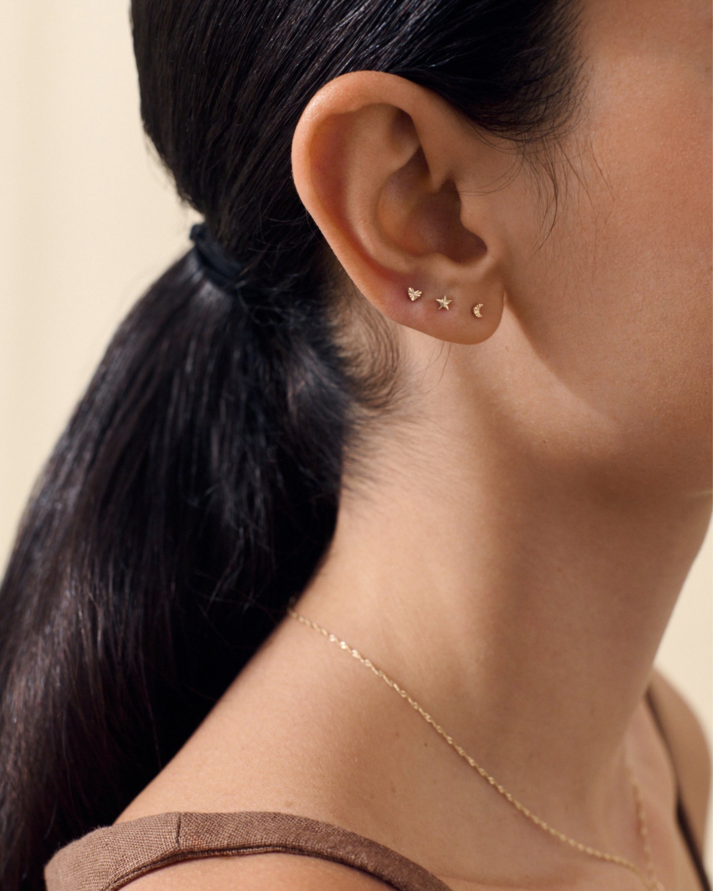 Close-up of a woman's ear wearing a Solid Gold Star Piercing Earring stud made from recycled solid gold, paired with delicate matching celestial-inspired studs, showcasing ethically sourced, fine jewellery designed for everyday elegance.