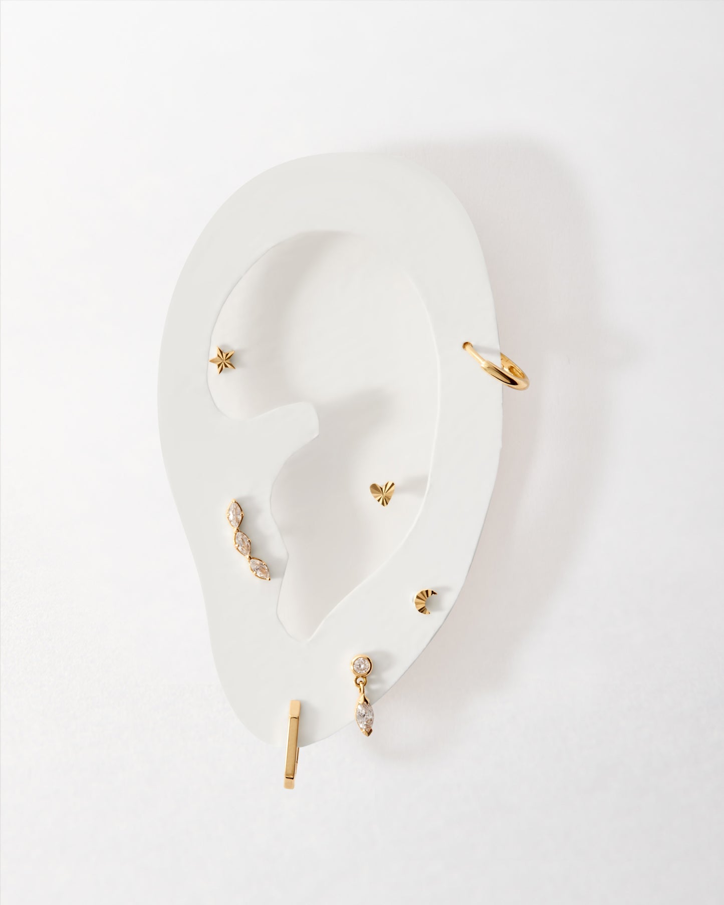 Solid Gold Star Piercing Earring displayed on a white ear model alongside other gold stud and hoop earrings, showcasing fine sustainable jewellery crafted from solid gold.