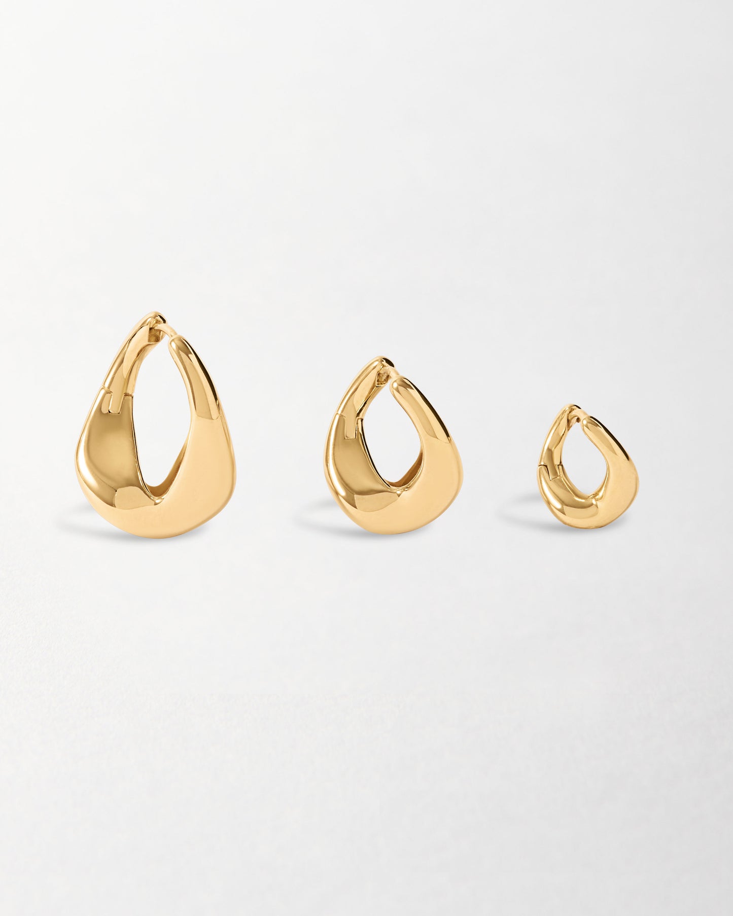 Three polished solid gold hoop earrings of varying sizes displayed on a white background, crafted from recycled metals with a smooth, modern twist design.