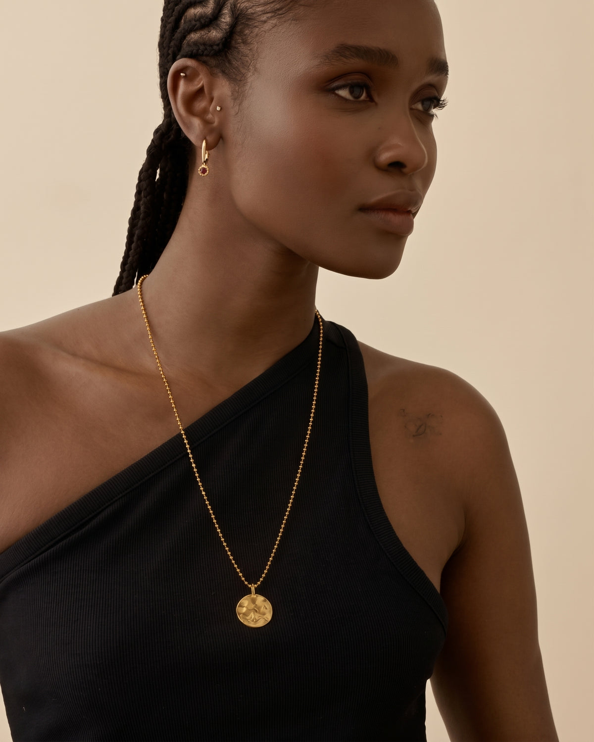 Coin Globe Necklace worn as a gold-plated pendant on a chain with a round globe coin design against a black top